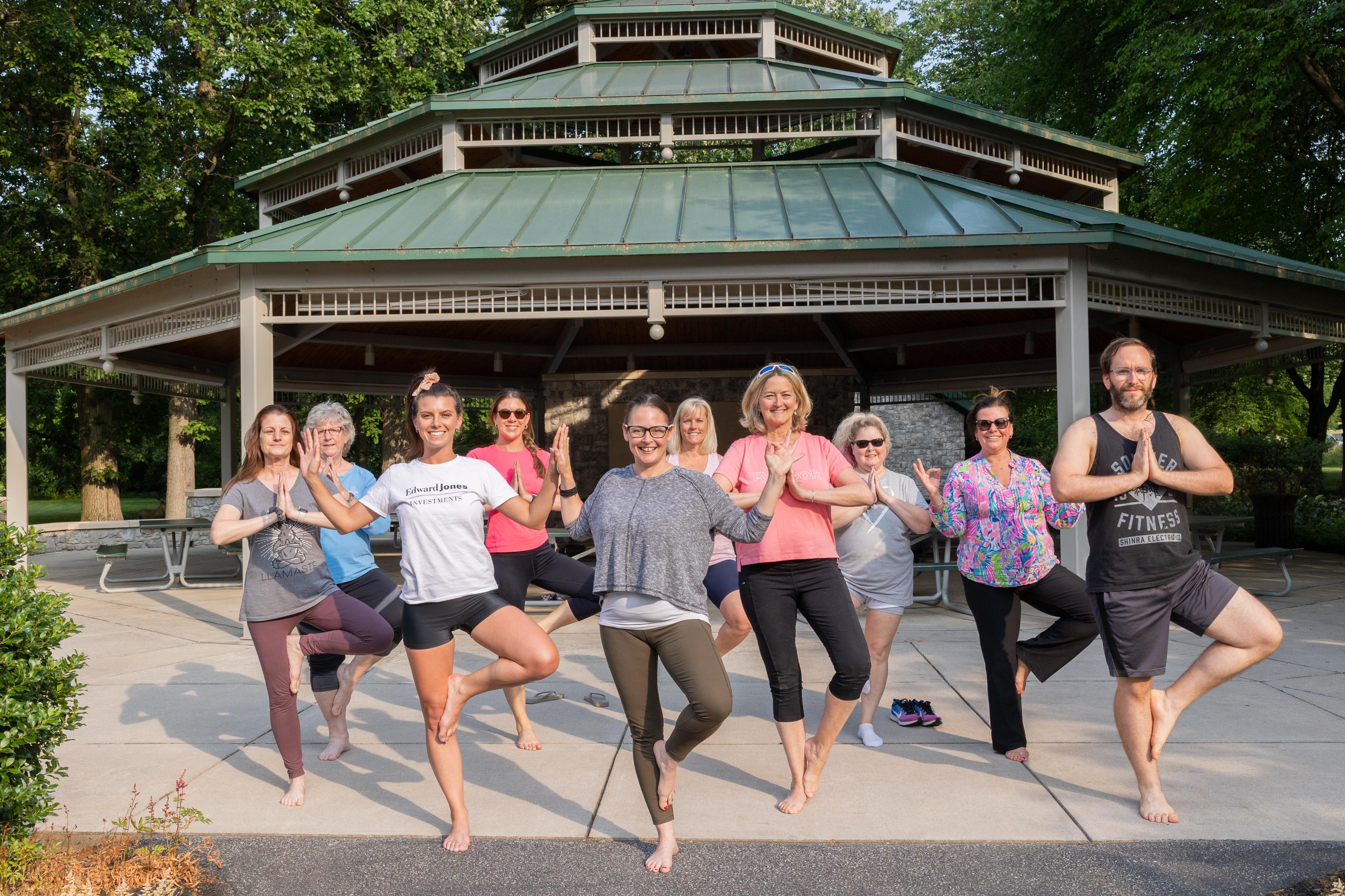Group of people doing yoga pose in front of a pavilion 