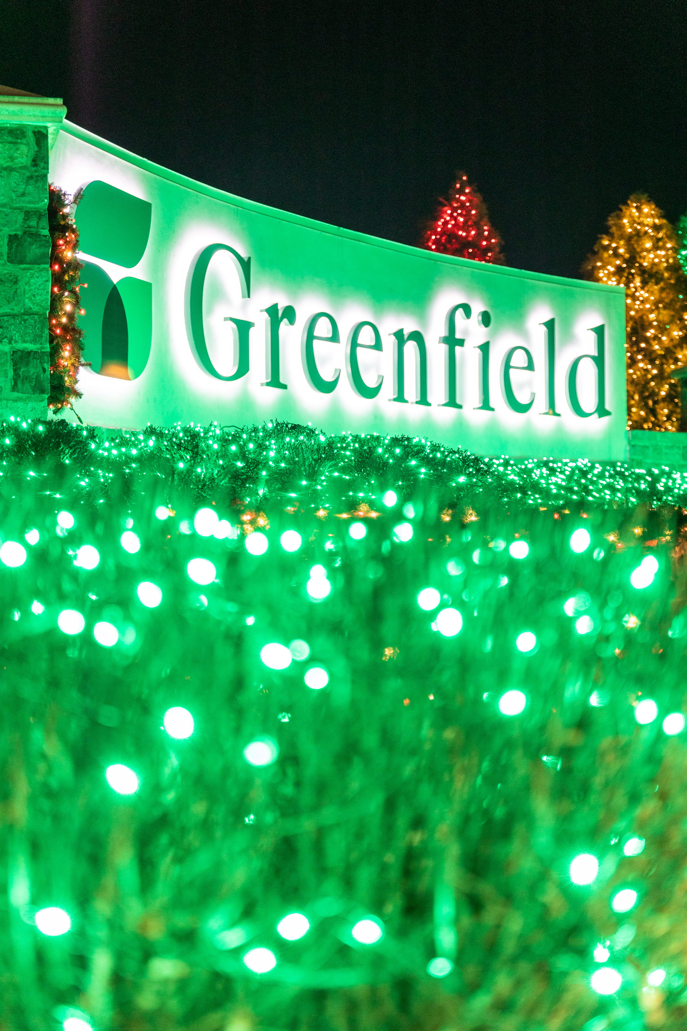 Greenfield Entrance sign illuminated with green holiday lights.