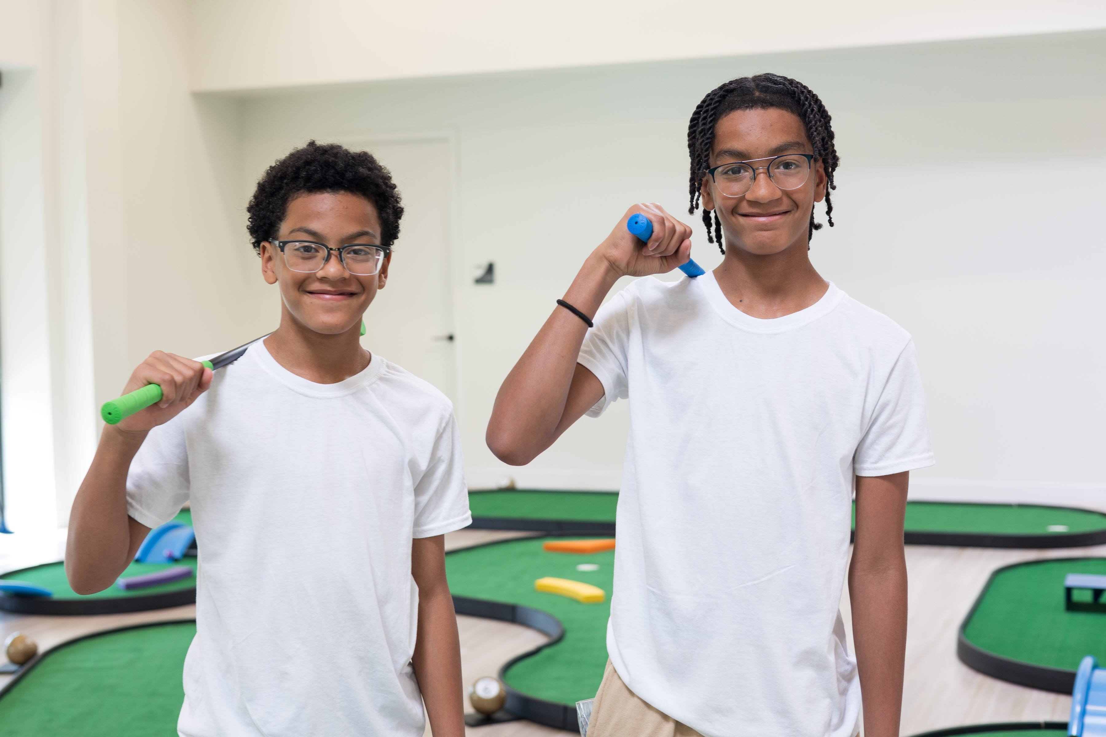 Two young boys smiling while playing mini golf 