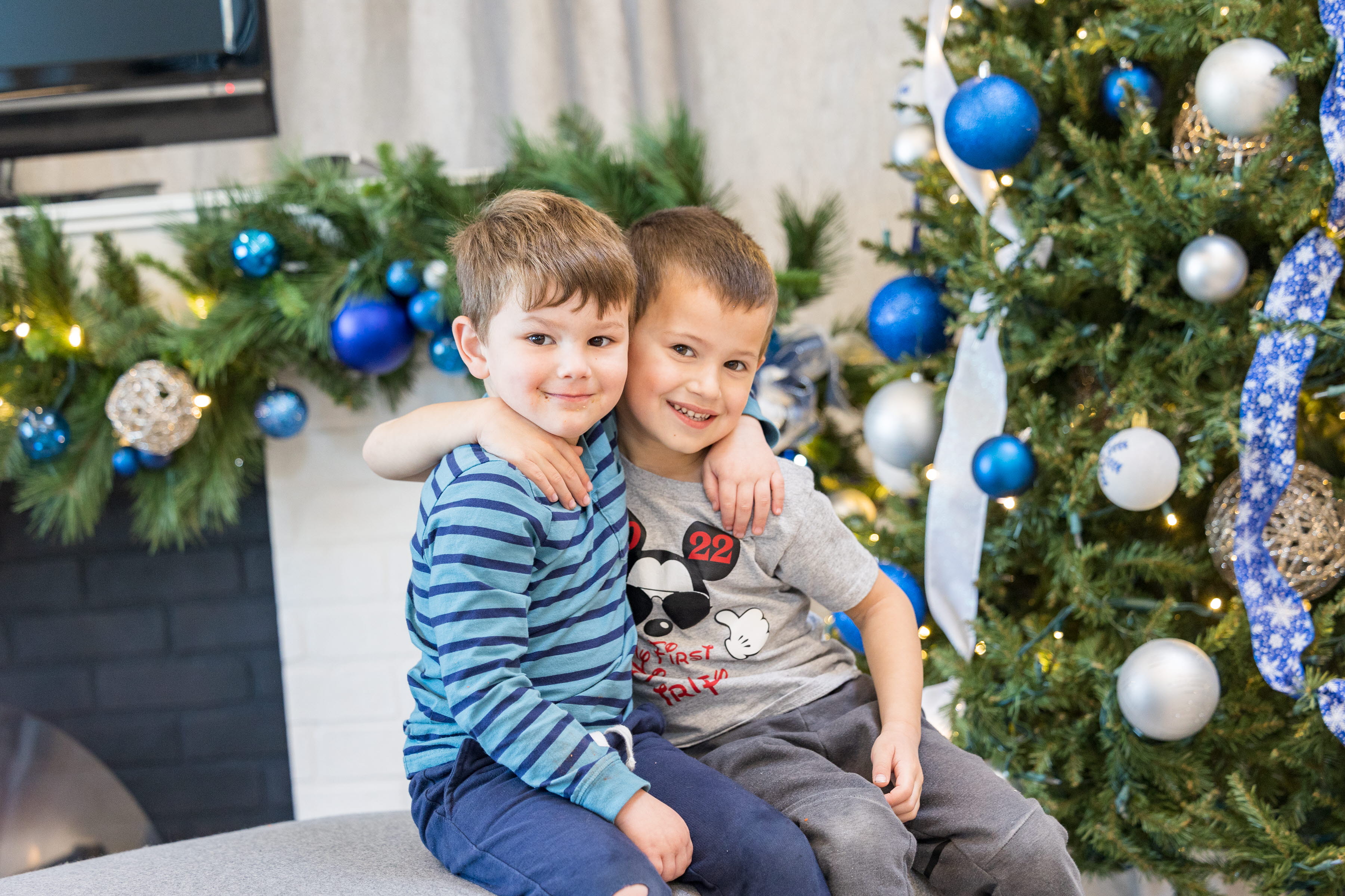 Two young male children hugging in from of Christmas Tree