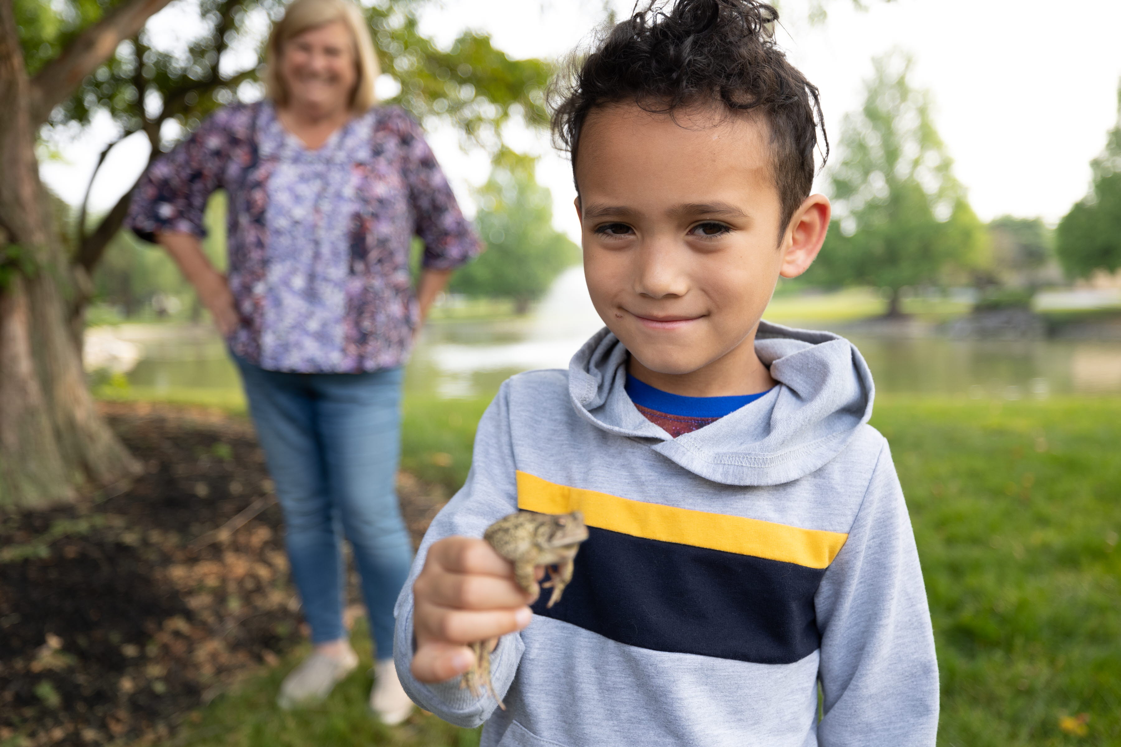 Young boy holding a frog with woman smiling the the background 
