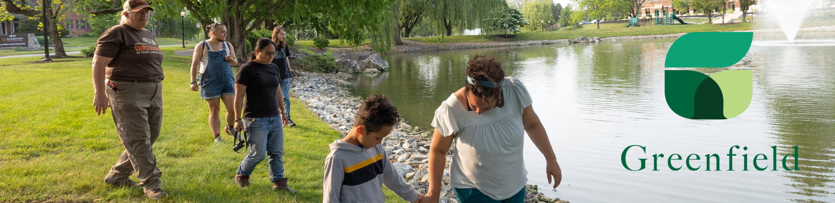 Group of people (adults and children) exploring a pond at Greenfield 